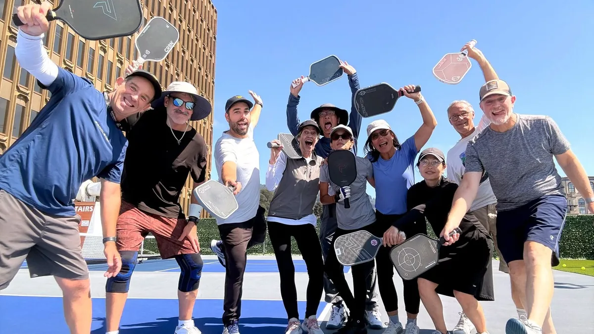 A dozen players crowded together on the rooftop court, paddles raised, cheering at the camera