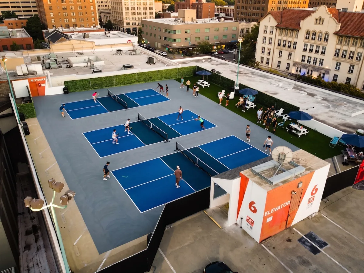Golden-hour drone view of the rooftop: games on all three courts, a crowd on the turf lounge under umbrellas, Downtown Berkeley behind